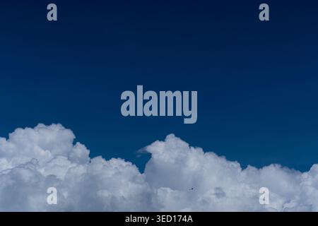 A panoramic-style photograph showing a thick layer of puffy white cumulus clouds at the bottom frame against a vast, clear deep blue sky. The composit Stock Photo