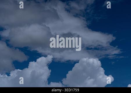 A dramatic close-up of layered clouds showing a mix of bright white cumulus and dark gray shadows against a deep blue sky. The photo highlights the de Stock Photo