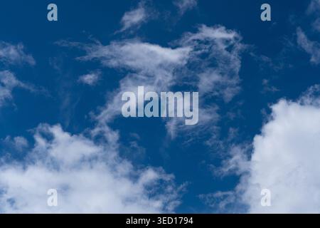A high-angle photograph showing a beautiful mix of wispy white clouds and soft cumulus formations scattered across a vibrant deep blue sky. The image Stock Photo