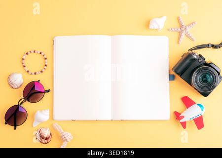 Open blank notebook with camera, sunglasses, toy airplane and travel accessories on yellow background. Top view summer vacation concept. Flat lay, moc Stock Photo