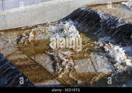 Ripples swirl in golden-brown hue beneath the cascade. The surface reflects sky and shadows, dynamic and alive Stock Photo
