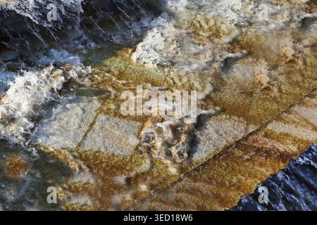 Golden hues swirl in frothy, dynamic motion. The surface glimmers under natural light. Ripples form across stone, creating fluid patterns Stock Photo