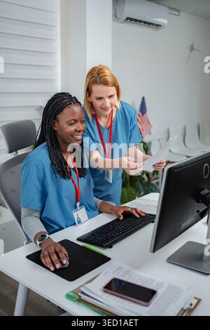 Two female nurses collaborating while looking at a desktop computer screen in a clinic Stock Photo