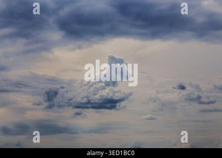 Single fluffy cloud breaks the gloom. Street lamps stand silent against the vast sky. Mood feels tense, expectant, heavy. Great for weather or urban m Stock Photo