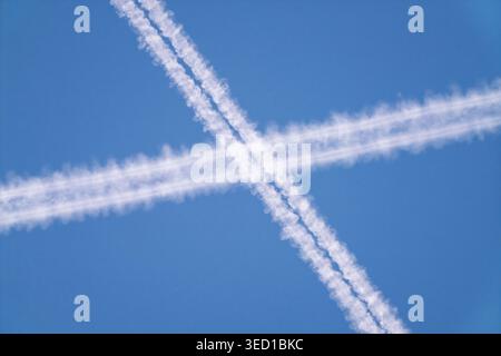 Jet trails crosswise. Distinctive vapors form striking X formations in blue sky Stock Photo