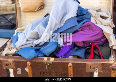 Open Vintage suitcase with a pile of old clothing inside for sale. England, UK Stock Photo