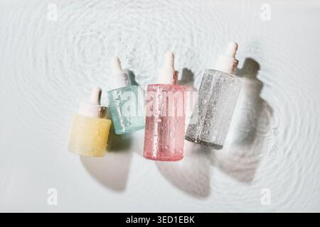 Dropper bottles with pastel skincare products reflecting light on gentle water surface Stock Photo