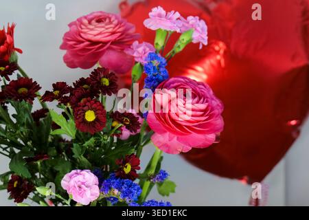 Vase of colorful flowers with a red heart balloon in the background, creating a bright Mothers Day composition. Stock Photo