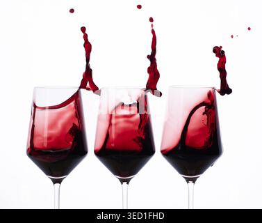 Red wine splashes create movement in three glasses in studio. Stock Photo