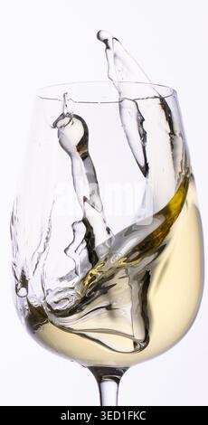 White wine splashes inside a clear wine glass. Stock Photo