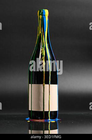 Liquid paints run down a wine bottle against black backdrop. Stock Photo