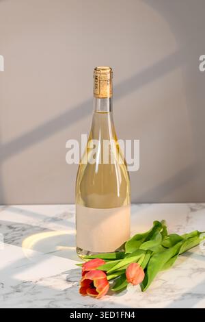 White wine bottle placed next to fresh tulips on surface Stock Photo