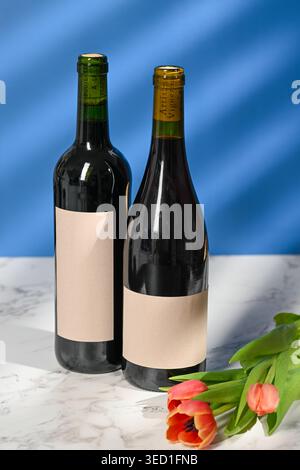 Two wine bottles with plain labels next to tulips on a table Stock Photo
