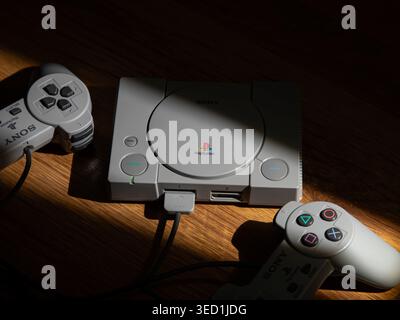 May 3, 2026, Odessa, Ukraine. Retro Sony PlayStation console with two controllers in dramatic sunlight on a wooden table. Stock Photo