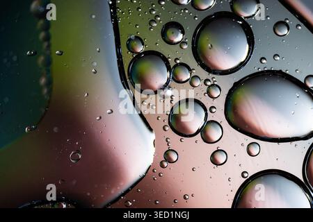 High contrast liquid droplets with sharp black outlines on a soft pink and green gradient Stock Photo