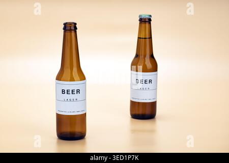 Two amber glass craft lager beer bottles featuring clean minimalist white rectangular labels with bold Beer Lager typography, placed on a smooth warm Stock Photo