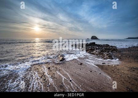 Sun setting behind Black Rock on Widemouth Bay Cornwall viewed at high tide Stock Photo