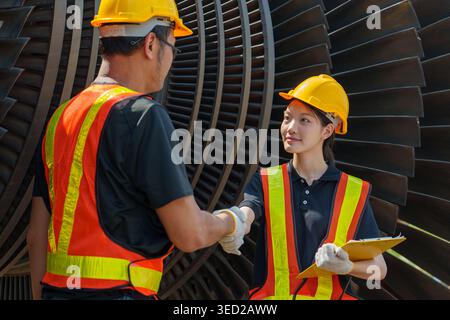 Asian male and female engineers shake hands after completing a turbine inspection at an industrial plant, illustrating professional teamwork and succe Stock Photo