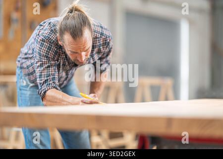 Woodworker precisely marking wooden board in carpentry workshop Stock Photo