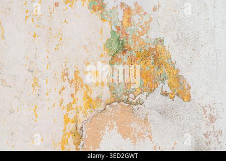 Cracked and peeling layers of colorful paint reveal the aged texture of an old plaster surface. Stock Photo