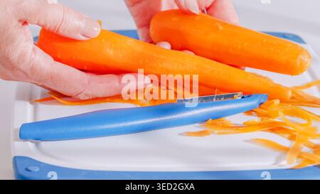 Peeled carrots being held over a peeler and cutting board. Stock Photo