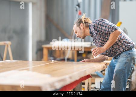 Man applying epoxy resin to wooden table in workshop Stock Photo