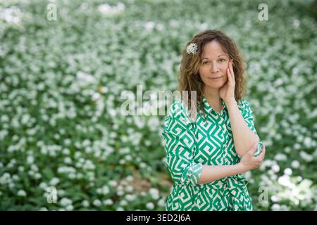 Intimate portrait of a woman in a green patterned dress with a wild garlic flower in her hair, standing against a beautiful, soft bokeh background of Stock Photo