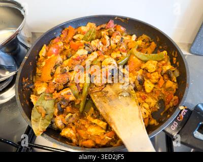 Chicken and bell pepper stir fry simmering in a frying pan with a wooden spatula on a kitchen stove Stock Photo