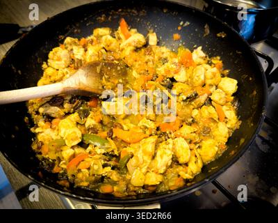 Chicken curry with vegetables and bell peppers cooking in a black wok on a kitchen stove with a wooden spoon Stock Photo