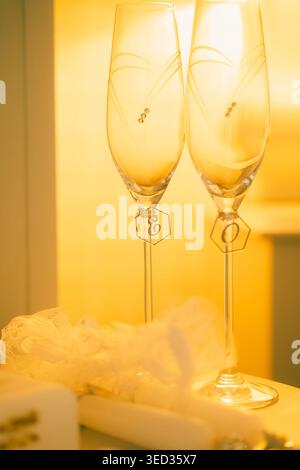 Elegant white heels prepared for  wedding celebration. White high heels sit beside two champagne glasses, small gift box, and decorative item. setting Stock Photo