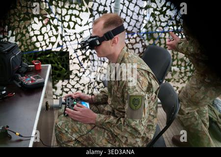 Soldier in camouflage uniform using FPV goggles and remote controller to pilot a drone, military tactical training for unmanned aerial vehicle Stock Photo