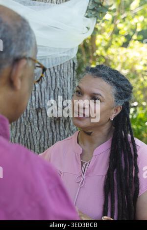African American couple standing by tree with sheer wrap, woman in pink blouse, man wearing glasses Stock Photo