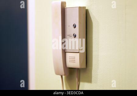 A modern intercom handset with two control buttons is mounted on a light green wall, representing a digital home entry system with communication and d Stock Photo