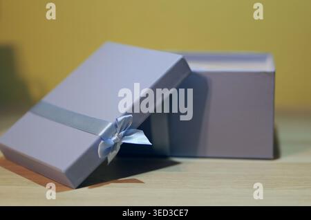 An open pastel gift box with a satin ribbon sits on a wooden surface, with a soft blurred background highlighting its minimalist elegant design. Stock Photo
