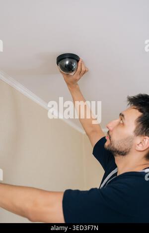 Professional technician installing modern dome style surveillance camera on residential or commercial ceiling, ensuring advanced personal or property Stock Photo