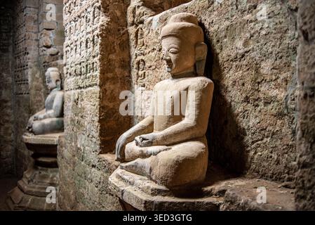 Side shot of ancient Buddha statues carved from light stone inside the corridors of Shittaung Temple in Mrauk U. The sacred figures sit in meditation Stock Photo