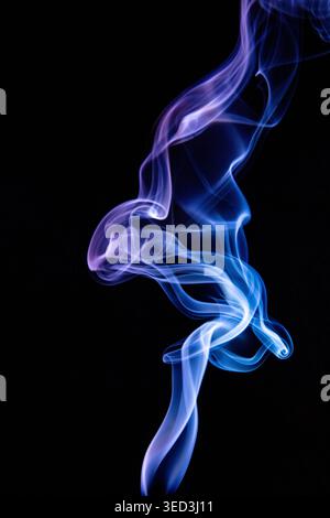 Blue smoke twists through dark air, revealing drifting particles and delicate vortices while forming an intriguing abstract with black background. Stock Photo