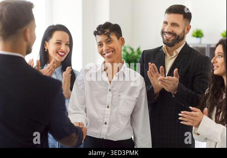 Happy team congratulating female colleague, shaking hands, applauding and celebrating success. Stock Photo