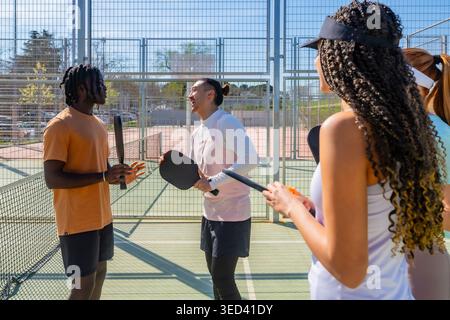Diverse friends laughing and playing pickleball on outdoor court Stock Photo