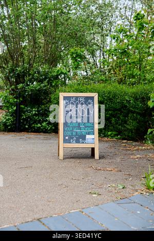 Chalkboard sign with a wooden frame standing outdoors on a sidewalk, displaying we are dog friendly and welcoming well behaved dogs amidst green bushe Stock Photo