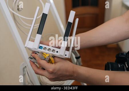 Close-up of hands holding modern white wireless router. Person connecting ethernet patch cords to ports for internet setup. Concept of home network Stock Photo