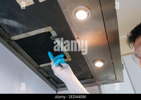 Person wearing protective gloves and safety glasses removes greasy stainless steel range hood filter for cleaning, emphasizing routine maintenance and Stock Photo