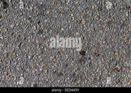 Dark asphalt surface featuring a rough texture of embedded stones and gravel Stock Photo