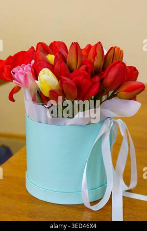 A blue box holds a variety of red and yellow flowers. It sits on a wooden table in an indoor setting. Stock Photo