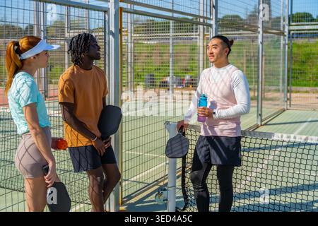 Diverse friends enjoying a conversation after playing pickleball on court Stock Photo