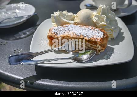 Warm apple strudel served with vanilla icecream and whipped cream at an outdoor cafe on a sunny day, dessert specialty from Austria, selected focus, n Stock Photo