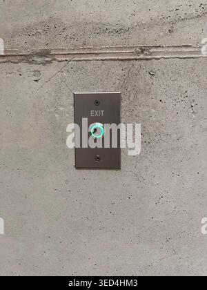 Minimal industrial interior detail with illuminated exit button mounted on raw concrete wall, modern architecture concept Stock Photo