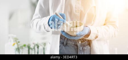 Scientist with mortar and plants in laboratory, closeup Stock Photo