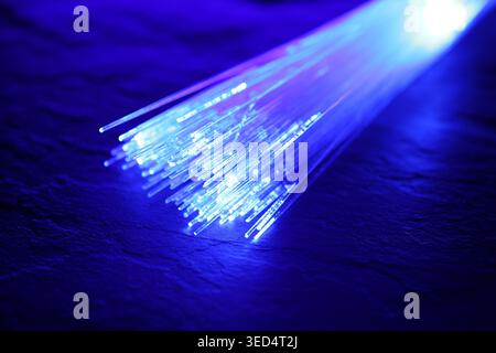 Optical fiber strands transmitting color light on textured background, closeup Stock Photo