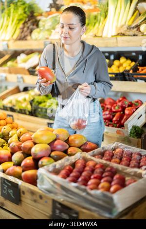 Young woman holding mango and bag in supermarket with vegetable and fruit display Stock Photo